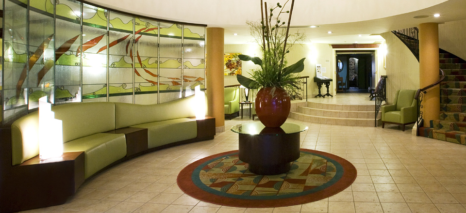 Lobby élégant d'hôtel avec canapé vert incurvé, mur décoratif en verre, plancher de tuiles et tapis rond à motifs, ambiance chaleureuse et accueillante